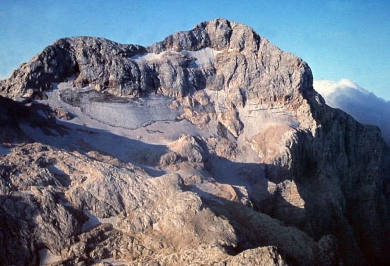 A photograph of a steep mountain slope scattered with smaller snow patches of varying sizes.