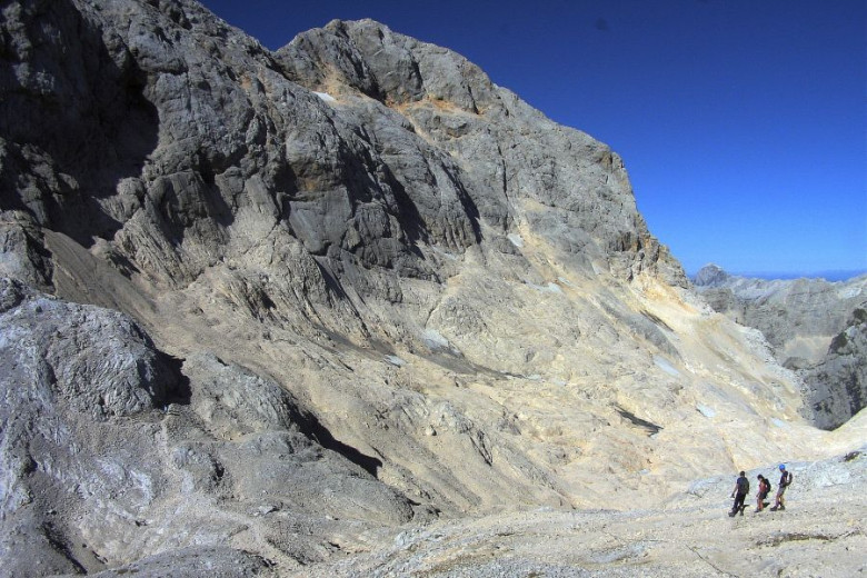 A grey steep mountain slope with a few patches of ice.