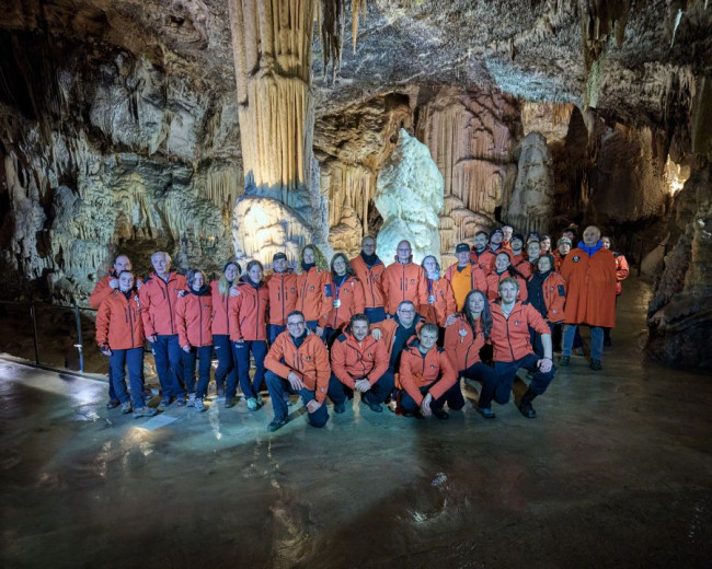 Cave guides in the orange uniforms in the front of the Postojna Cave symbol - a stalagmite called the Brilliant