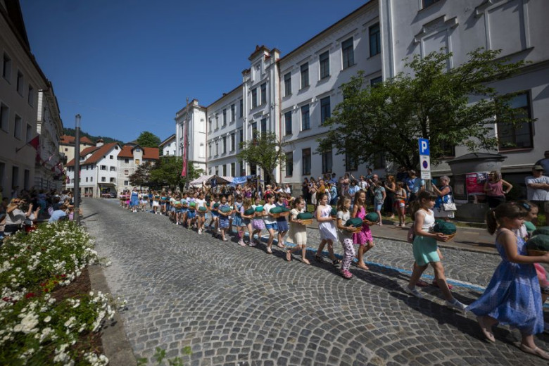 A long row of children, carrying bobbin lace pillows in the middle of a paved street.