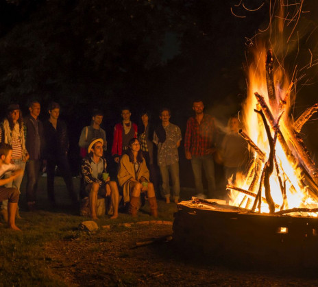 A burning bonfire and a group of people sitting and standing in halfcircle in the background.