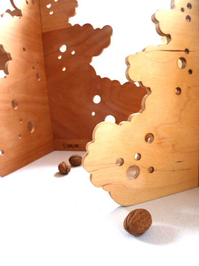 Detail of two Christmas trees carved from wooden panels with holes for decoration and three walnuts on the table.