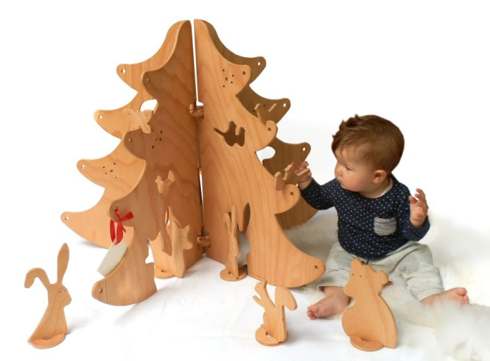 A wooden Christmas tree with the pieces of an animal puzzle. A child is sitting near tree and fitting forest animals into the openings.