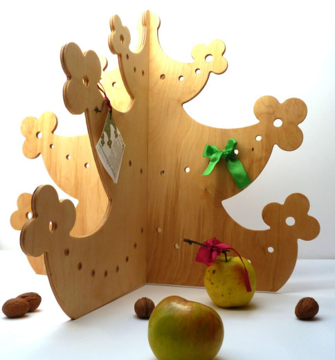 A Christmas tree carved from wooden panels, with branches in the shape of flowers. There are two apples and three walnuts next to it. 