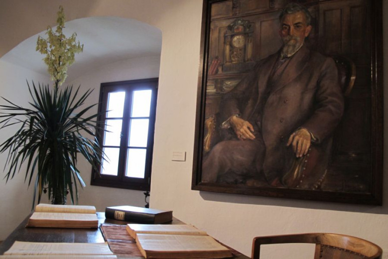 A table with a chair, a painted portrait of Ivan Tavčar hangs on the wall.