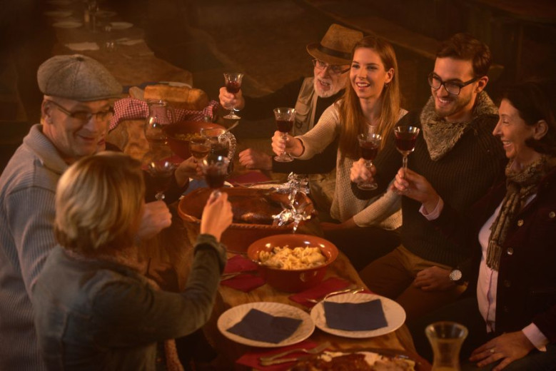 Ljudje za mizo, na kateri so z martinovo značilne jedi, nazdravljajo z vinom.