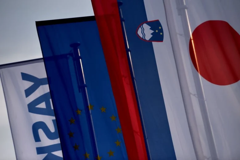 A row of flags of Japan, Slovenia, EU, and Yaskawa, waving in the wind.