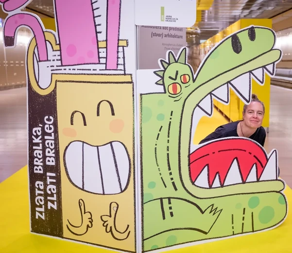 A person peeks through an opening in an illustrated display featuring a green crocodile with its mouth open.