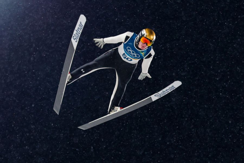 Ski jumper mid-air at night, wearing a black and white suit with the number 50. The athlete's form is dynamic, displaying grace and precision. 