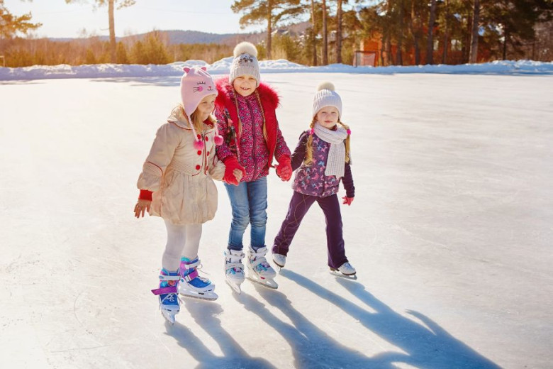 Three little girls are skating together and holding each other with the hands