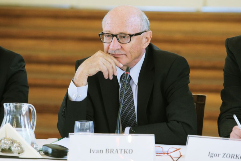 Ivan Bratko, wearing glasses and a dark suit, sitting at a table with name cards and a microphone.
