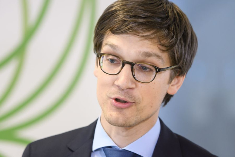 Close-up of Jure Leskovec, wearing glasses, dark suit, light blue shirt, and a darker blue tie. He appears to be speaking.
