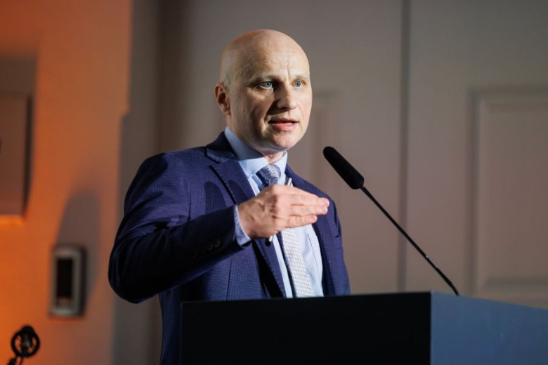 Kozma Ahačič at a podium, wearing a blue suit, addressing an audience.