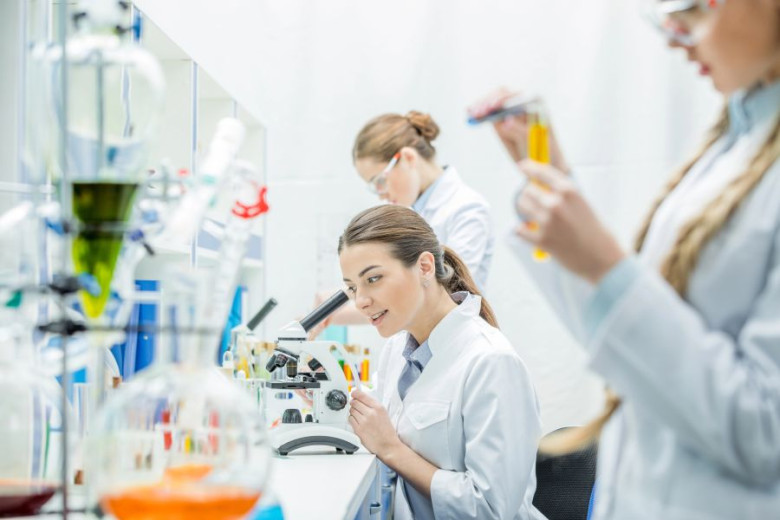 Three scientists in a lab, one using a microscope, another holding a test tube.