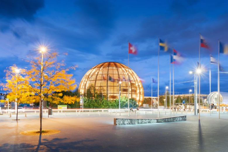 The Globe of Science and Innovation building at CERN, illuminated at twilight, with international flags in the background.