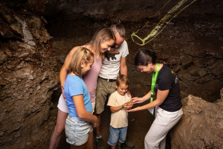 A guide shows an animal bone remain to an attentive family of four in a dimly lit cave.