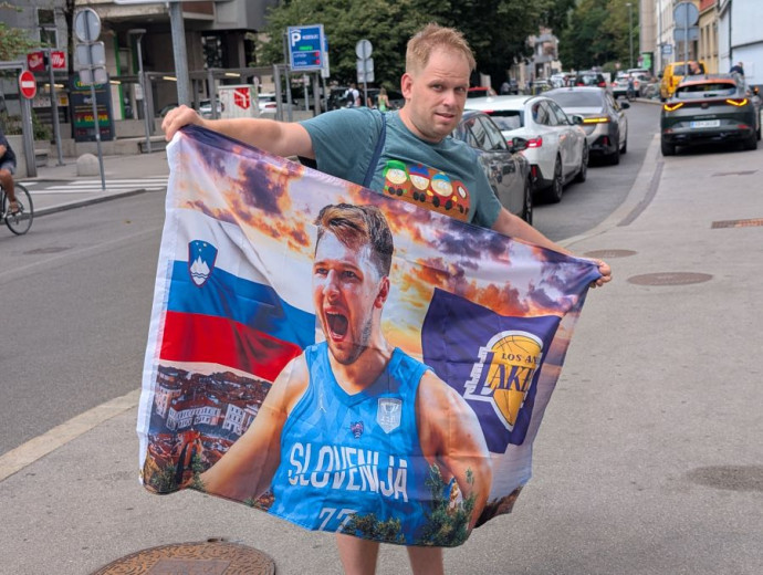 A fan holding a Luka Dončić banner, with Slovenian and LA Lakers flags in the background.