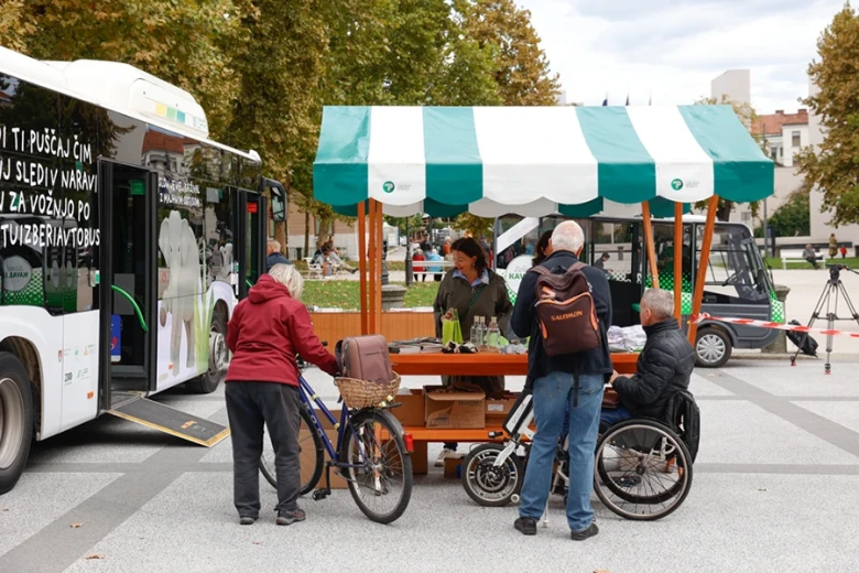 People gather around an accessible city bus and a booth in a public square.