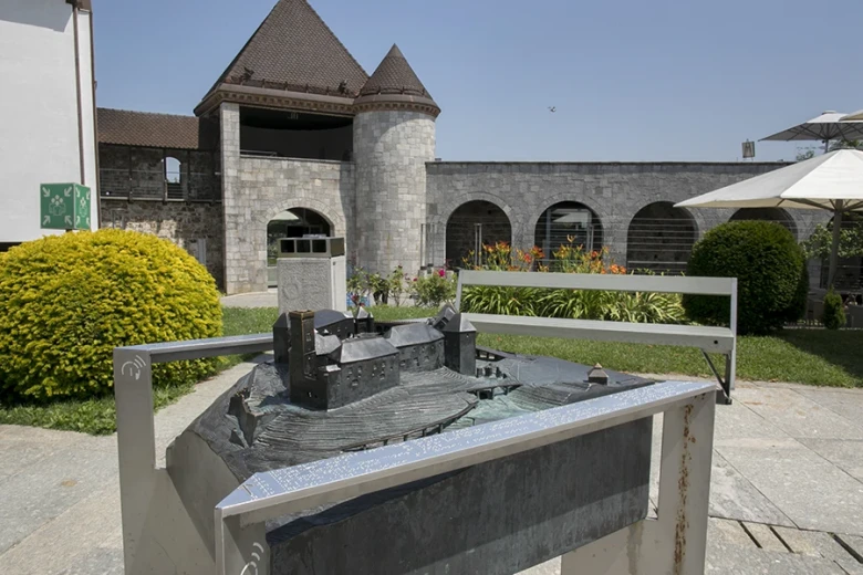 A tactile model of a castle stands outdoors in front of the castle building.