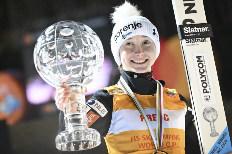 Nika Prevc is holding a crystal trophy in one hand and skis in the other.