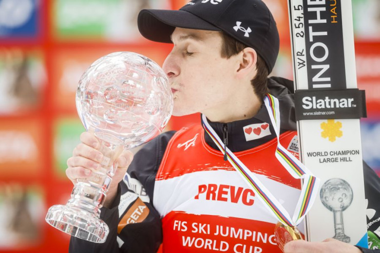 Ski jumper Domen Prevc kisses a large crystal trophy and holding his skis.