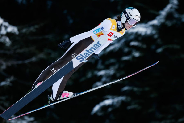Ski jumper in mid-air, wearing white and black gear.