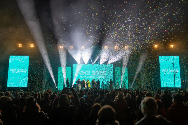Confetti shower at an event with stage lights and screens showing 'Go! 2025 Nova Gorica Slovenia'