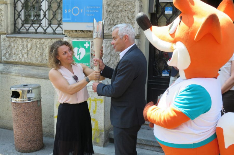 Saša Arsenovič hands the Flame of Peace to Ilka Štuhec. A mascot Foksi stands next to them.