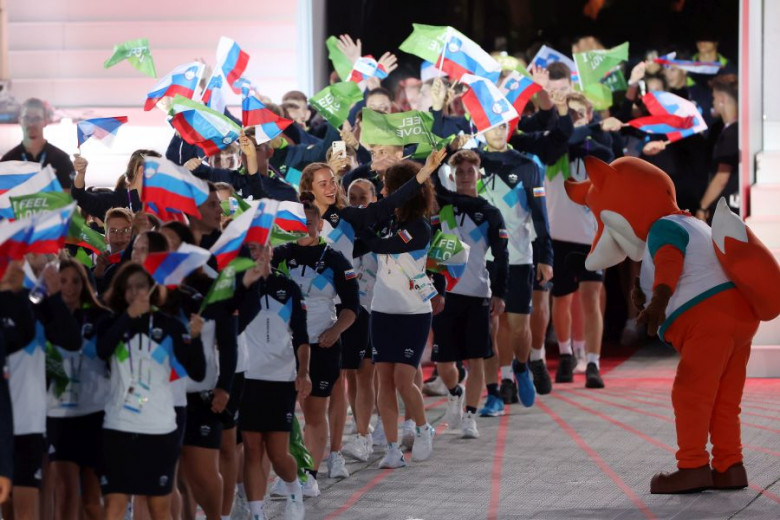 A parade of young athletes with Slovenian and I feel Slovenia flags. The mascot Foksi greets them.