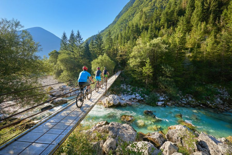 Three cyclists cycle on a bridge over the Soča River.