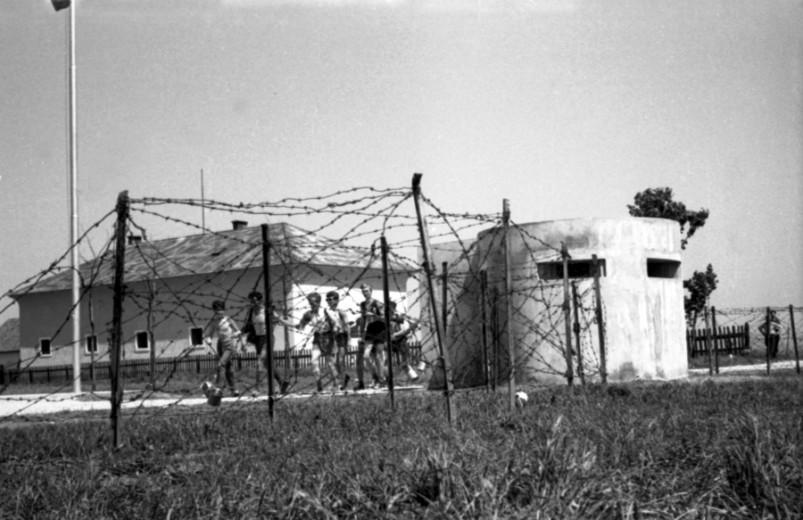 A group of young man running on a path along the barbed wire and a bunker.