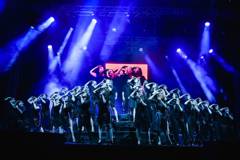 Group of singers performing on the stage with strong blue reflectors above.