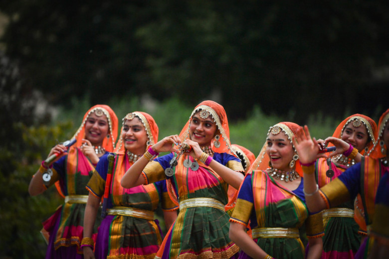 Performers dressed in colorful traditional costumes. They look happy and some are showing hearts with their fingers.