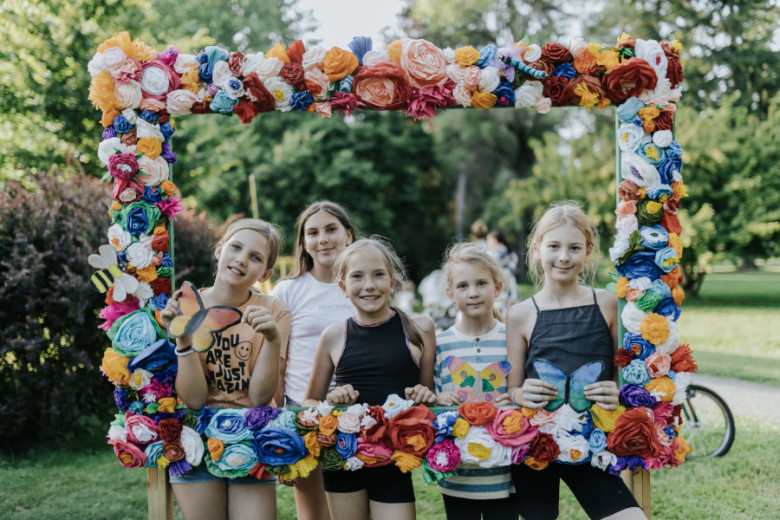 Children are taking photo with big floral frame. The background is filled with nature.
