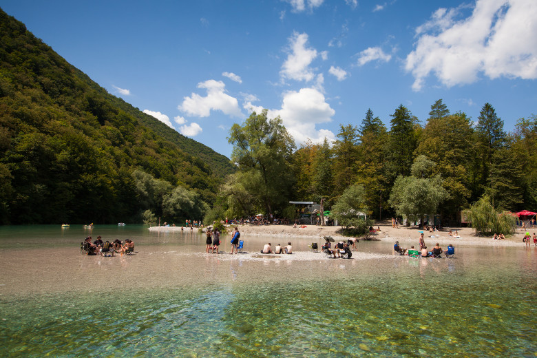 People swimming and socialising by the Soča River.