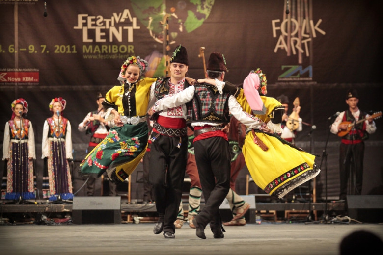 Couples in national costumes dancing on stage. Musicians playing, women singing.