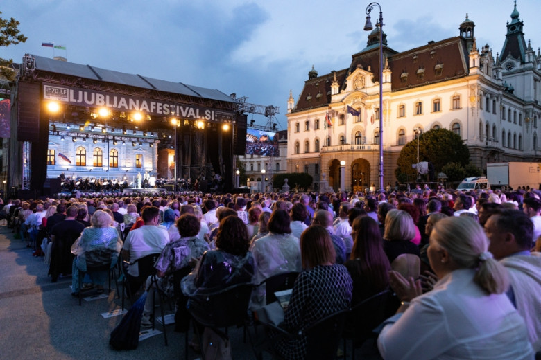 Obiskovalci Ljubljana festivala sedijo na Kongresnem trgu in spremljajo nastop na odru.