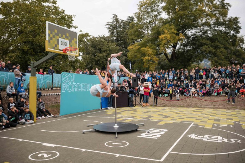 Two female acrobats are dancing on a pole on a basketball court.