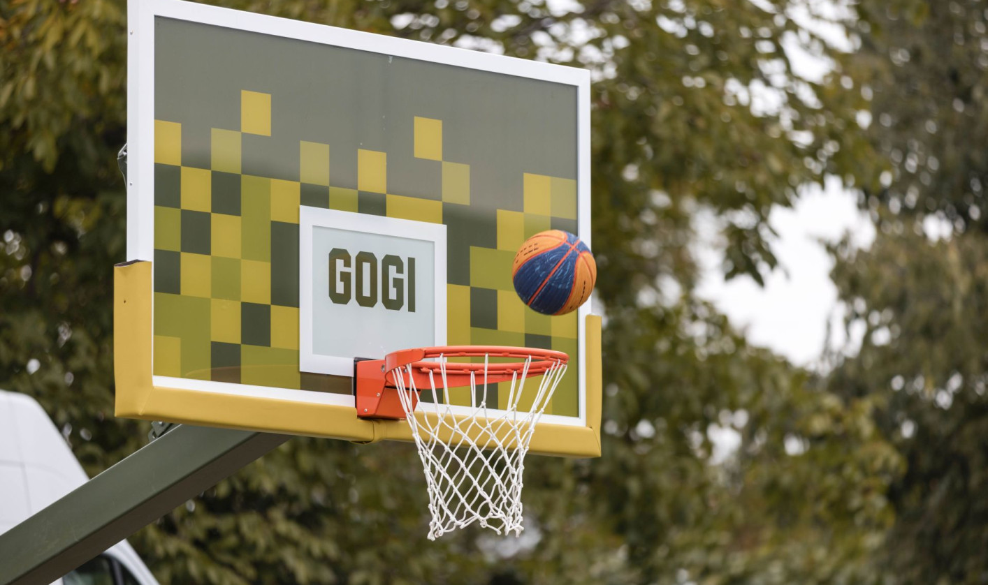 A ball is flying into a basketball hoop with a sign GOGI on it.