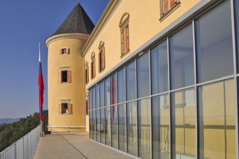 A view of the side section of the renovated castle with part of one tower visible, featuring large modern windows and the Slovenian flag on the towe