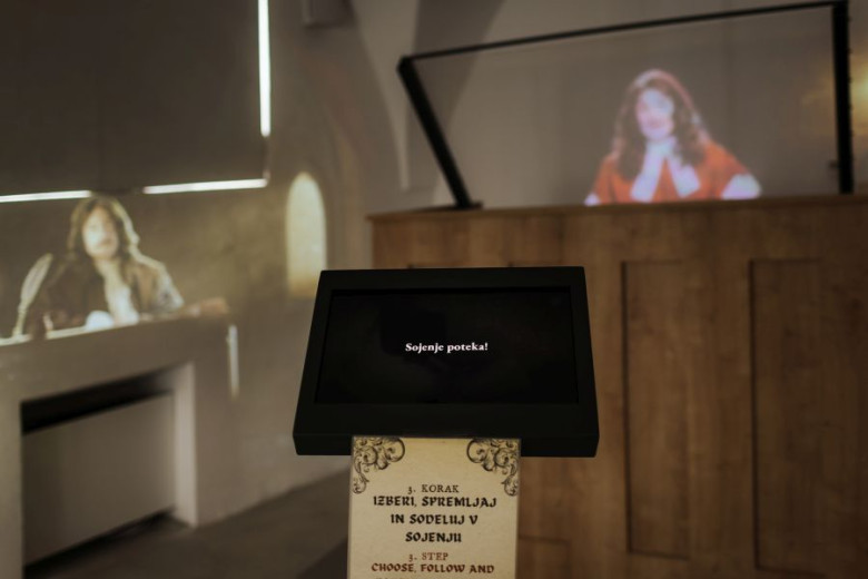 The room shows a courtroom with a wooden desk. Two judges are projected on the walls, and in front of them, a screen says that the trial is starting.