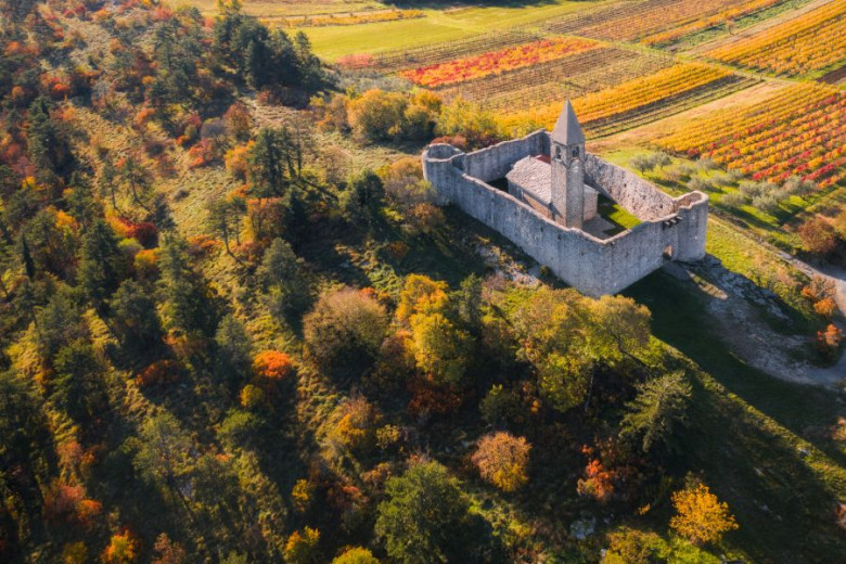 Pogled z zraka na kamniti grad, obdan z jesenskim gozdom in pisanimi polji.