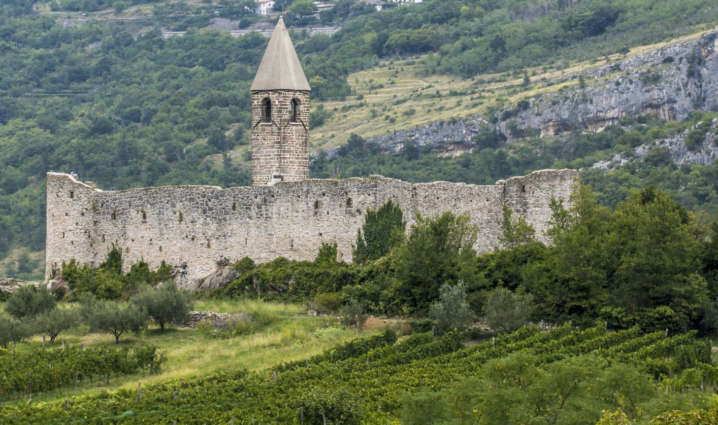 Kamnit zid z visokim stolpom nad vinogradi in zelenimi griči.