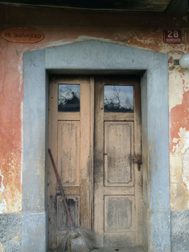 Stara hiša js starimi vrati in napisanim hišnim imenom na glineni tablici Skrivenjko zaradi tega ker je skrita v gozdu 