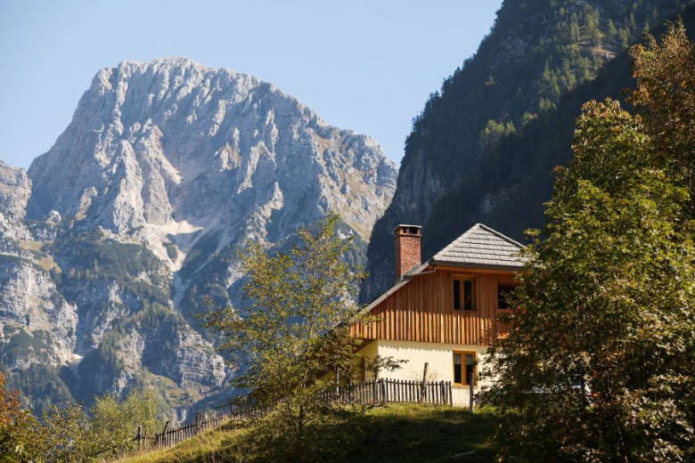 Lesena gorska hiša v lesu in z belo fasado v ozadju pa so gore