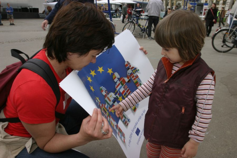 A lady shows a poster of EU flags to a child.
