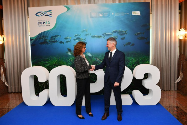 Robert Golob and Maša Kociper shaking hands in front of the COP 23 billboard.