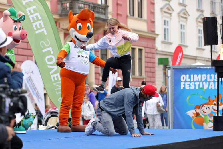 The mascot Foxes stands on stage. A girl is jumping over a boy.