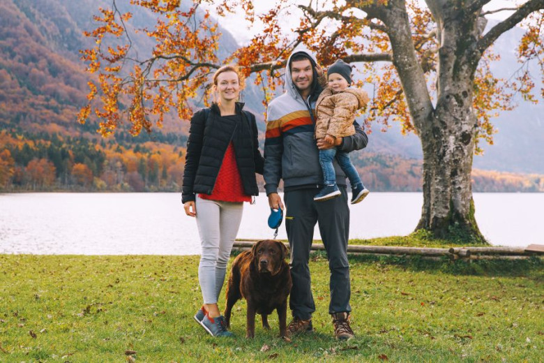 A couple with a child and a dog standing by Lake Bohinj.