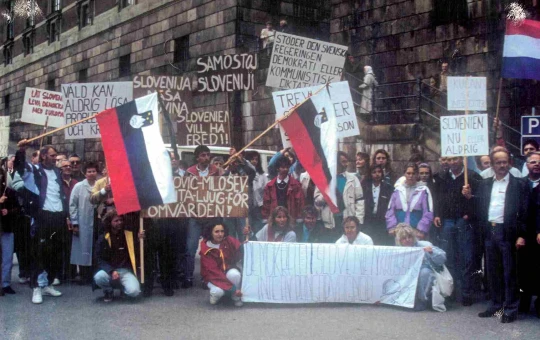 A huge crowd of smiling women in Slovenian national costumes at a demonstration are waving Slovenian flags and holding up banners with "Thank you Australia" written on them.